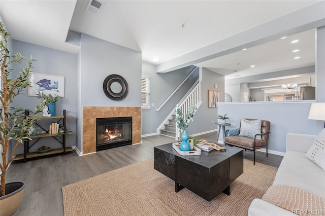 living room with visible vents, baseboards, stairway, a tile fireplace, and wood finished floors