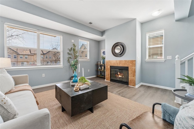 living room with a tiled fireplace, wood finished floors, baseboards, and a healthy amount of sunlight