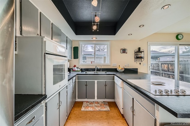 kitchen with sink, gray cabinetry, a raised ceiling, dishwasher, and light hardwood / wood-style floors