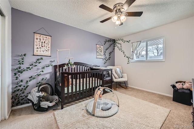 carpeted bedroom featuring a crib, ceiling fan, and a textured ceiling