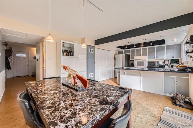 kitchen with stainless steel microwave, glass insert cabinets, oven, light wood-type flooring, and a peninsula