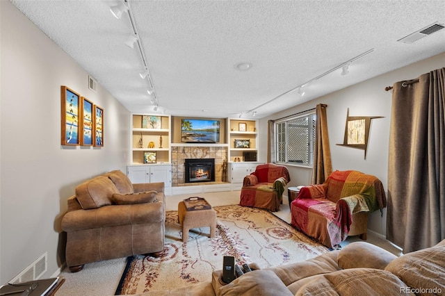 carpeted living room with built in shelves, a stone fireplace, a textured ceiling, and rail lighting