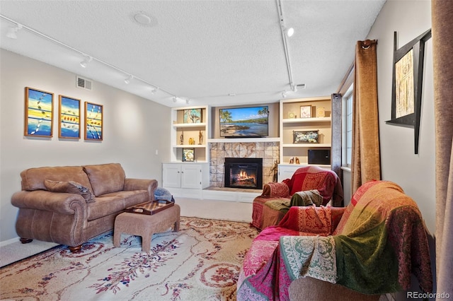 living room with track lighting, a stone fireplace, carpet, and a textured ceiling