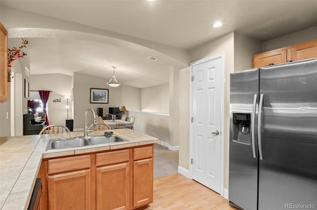 kitchen featuring tile countertops, decorative light fixtures, sink, stainless steel refrigerator with ice dispenser, and light wood-type flooring