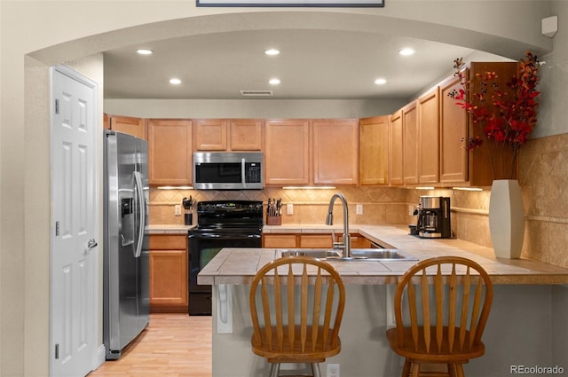 kitchen featuring sink, a kitchen bar, kitchen peninsula, stainless steel appliances, and light wood-type flooring