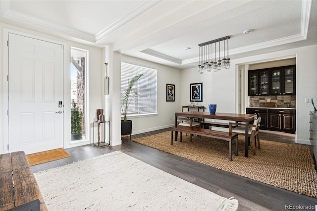 dining room with a raised ceiling, crown molding, dark wood-type flooring, and indoor bar