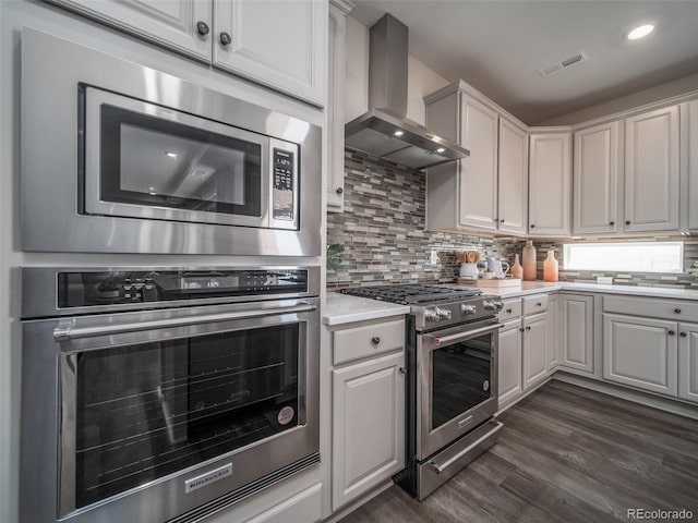 kitchen with appliances with stainless steel finishes, wall chimney exhaust hood, and white cabinets