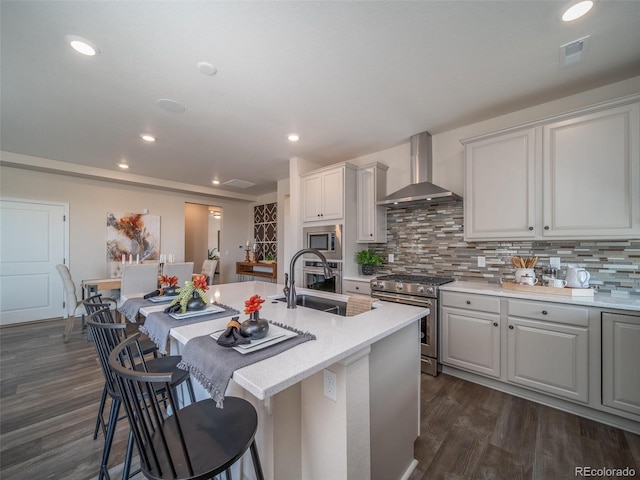 kitchen featuring a center island with sink, appliances with stainless steel finishes, sink, and wall chimney range hood