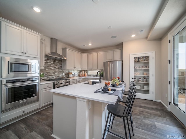 kitchen featuring wall chimney exhaust hood, sink, high end appliances, a kitchen island with sink, and white cabinets