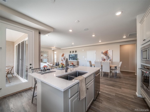 kitchen featuring sink, dark wood-type flooring, appliances with stainless steel finishes, white cabinetry, and a center island with sink