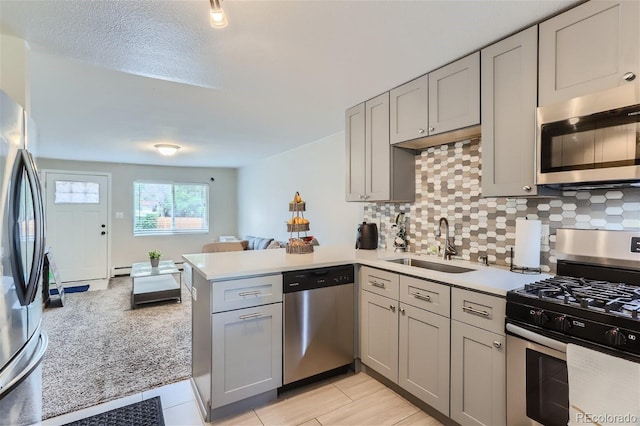 kitchen featuring a peninsula, gray cabinets, a sink, stainless steel appliances, and light countertops