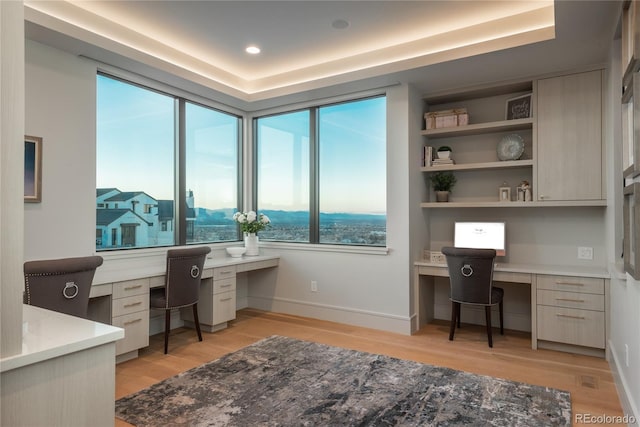 office space with baseboards, plenty of natural light, built in desk, and light wood-style floors