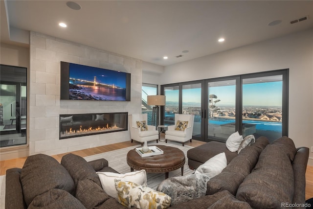 living room with a tiled fireplace, recessed lighting, wood finished floors, and visible vents