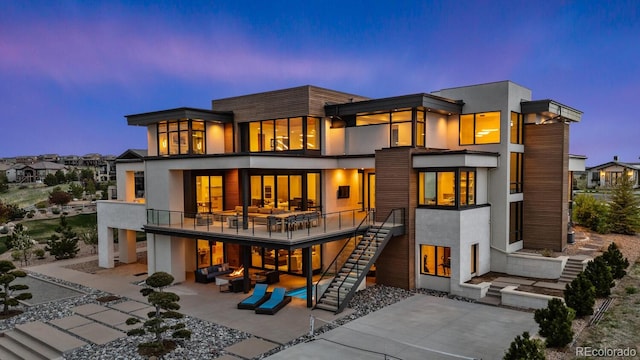 back of property at dusk with a patio, stucco siding, a balcony, and stairway
