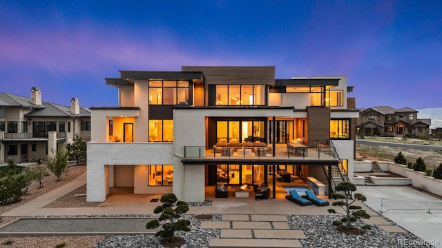 back of house at dusk featuring stairway, a balcony, and a patio area