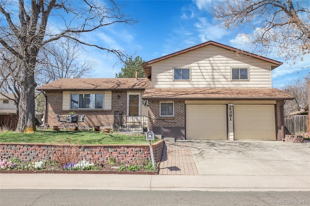tri-level home with concrete driveway, a front lawn, an attached garage, brick siding, and fence