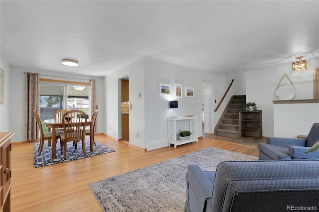 living room featuring visible vents, baseboards, stairway, and light wood finished floors