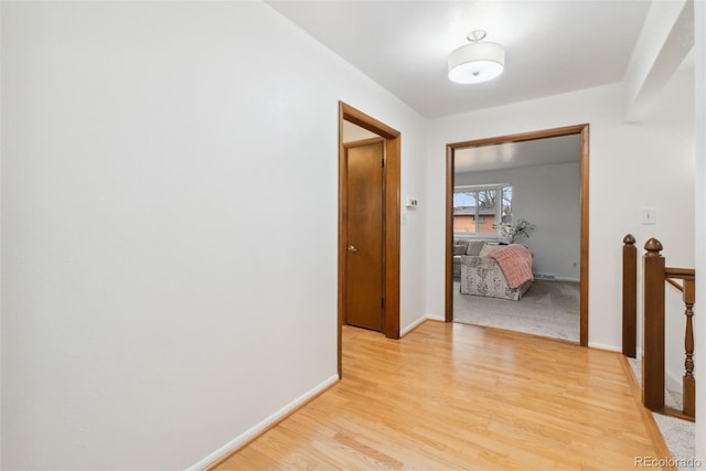 hall featuring light wood-style flooring, an upstairs landing, and baseboards