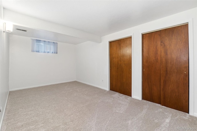 unfurnished bedroom featuring carpet flooring, visible vents, and multiple closets