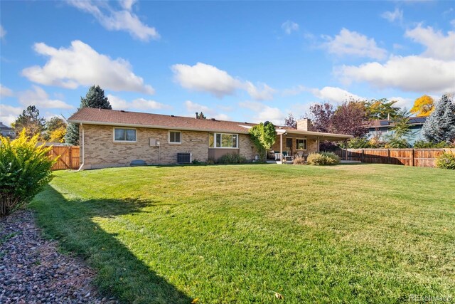 rear view of house with brick siding, a lawn, cooling unit, a chimney, and a fenced backyard