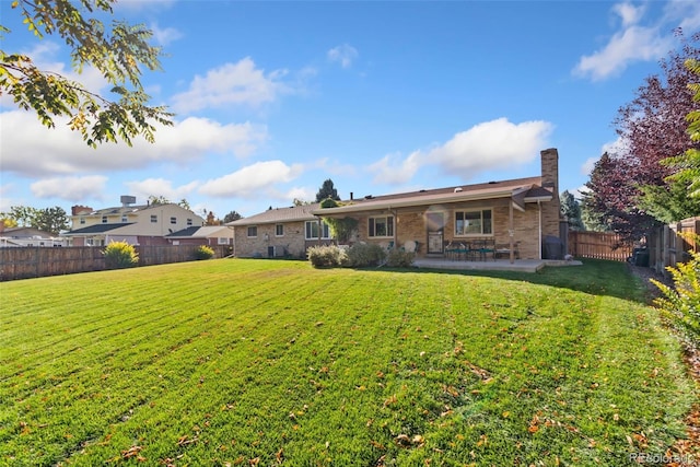 back of house with a patio, a lawn, a fenced backyard, and a chimney