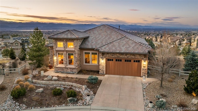 view of front of property featuring stone siding, fence, concrete driveway, a garage, and a tiled roof