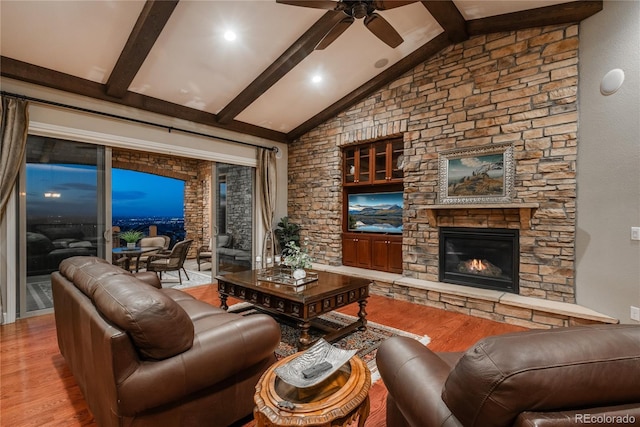 living area with a stone fireplace, wood finished floors, vaulted ceiling with beams, and a ceiling fan