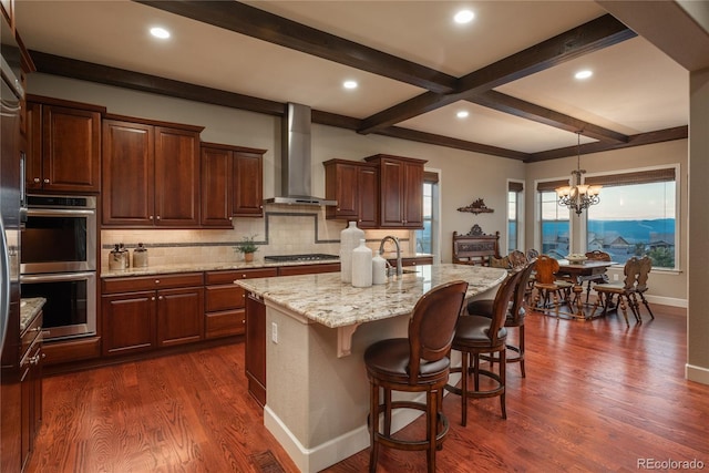 kitchen with dark wood-type flooring, wall chimney range hood, beamed ceiling, and stainless steel appliances