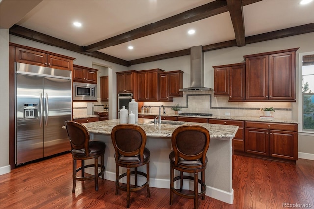 kitchen with built in appliances, dark wood-style flooring, wall chimney range hood, and a sink