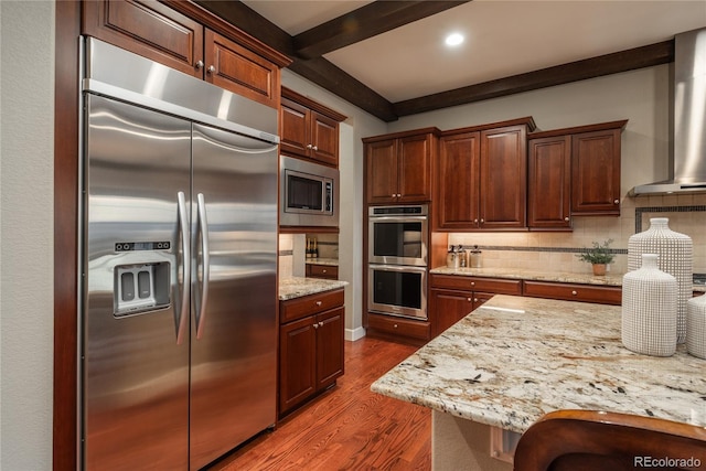 kitchen featuring tasteful backsplash, dark wood finished floors, built in appliances, beamed ceiling, and wall chimney exhaust hood