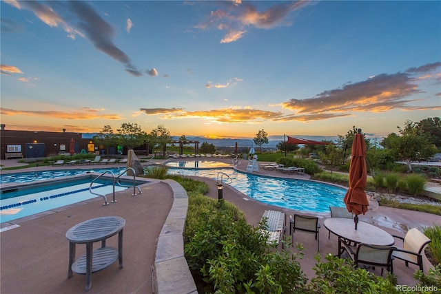 pool at dusk with a patio and a community pool