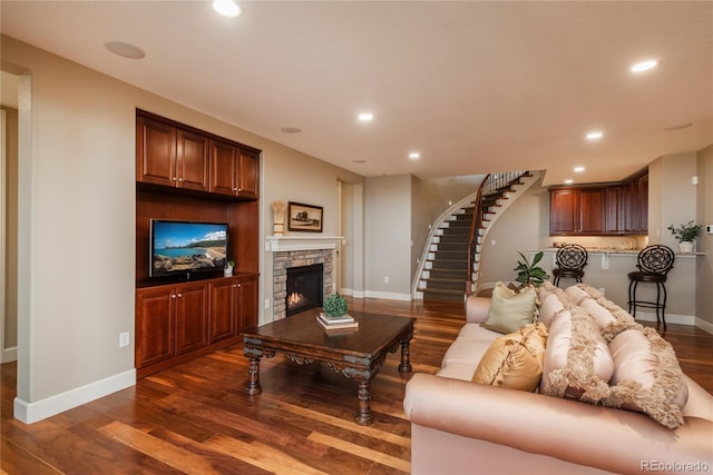 living area featuring baseboards, stairs, a stone fireplace, recessed lighting, and wood finished floors