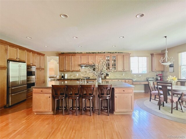 6035 S Paris St, Englewood, CO 80111 - kitchen with stainless steel appliances, light wood-type flooring, a center island with sink, a kitchen breakfast bar, and decorative backsplash