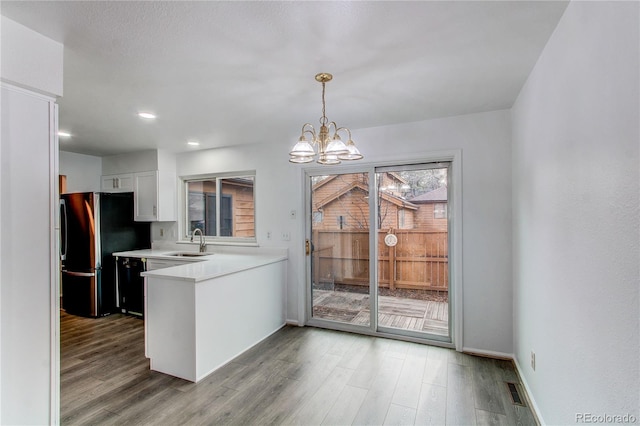 kitchen featuring sink, an inviting chandelier, stainless steel refrigerator, hardwood / wood-style floors, and white cabinets