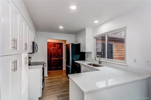 kitchen with appliances with stainless steel finishes, white cabinetry, sink, kitchen peninsula, and light stone countertops