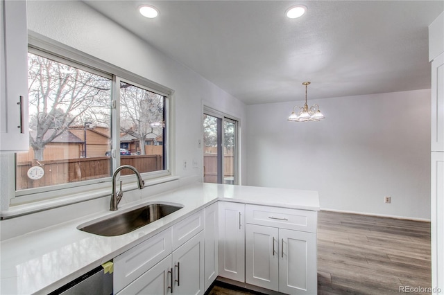 kitchen with sink, white cabinetry, decorative light fixtures, stainless steel dishwasher, and kitchen peninsula