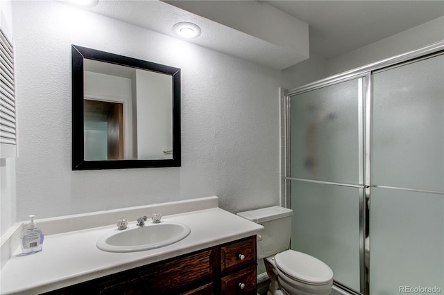 bathroom featuring a shower with door, vanity, and toilet