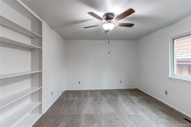 carpeted empty room with a textured ceiling, ceiling fan, and built in shelves