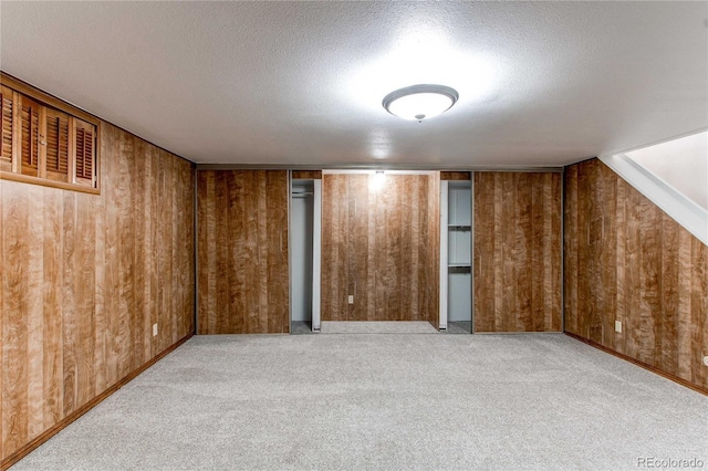 bonus room featuring wooden walls, light colored carpet, and a textured ceiling