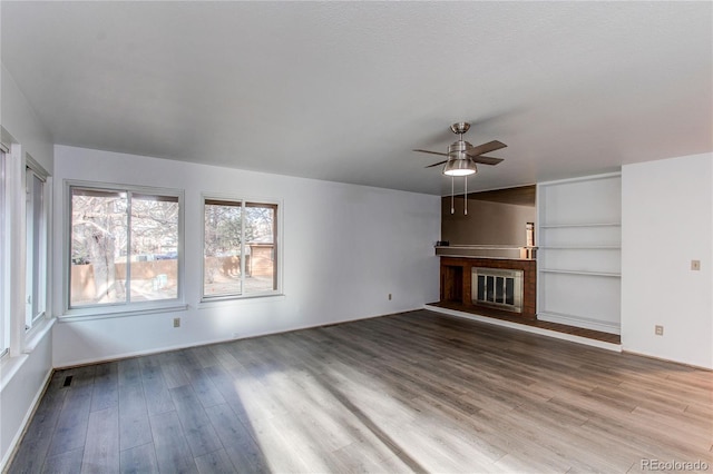 unfurnished living room featuring ceiling fan, wood finished floors, and a glass covered fireplace