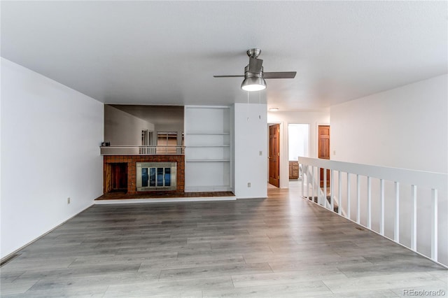 unfurnished living room featuring a brick fireplace, light wood finished floors, and a ceiling fan