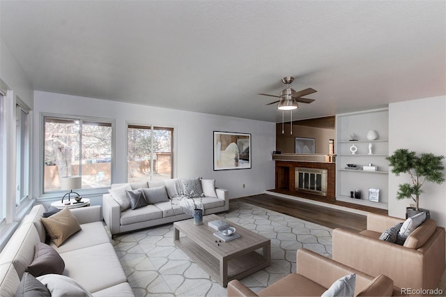 living area with built in shelves, a ceiling fan, wood finished floors, and a glass covered fireplace