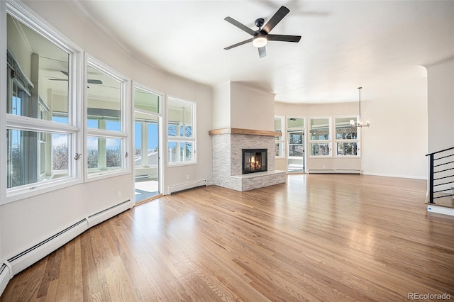 unfurnished living room featuring a baseboard heating unit, ceiling fan with notable chandelier, a fireplace, and wood finished floors