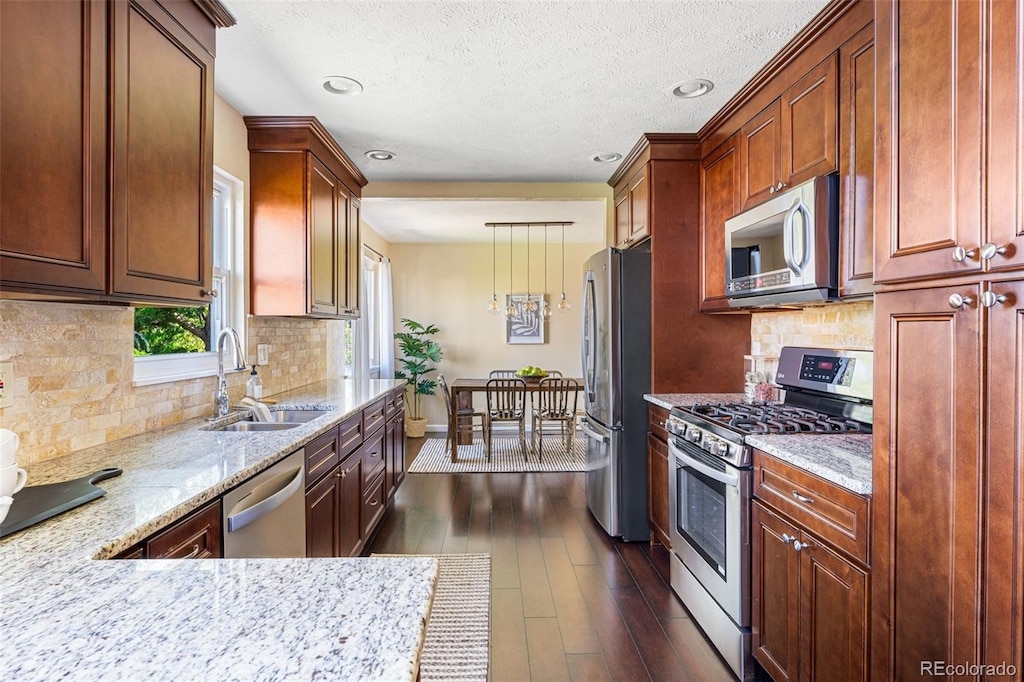 kitchen with sink, appliances with stainless steel finishes, dark hardwood / wood-style floors, pendant lighting, and light stone countertops