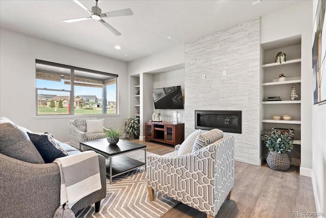 living area with a fireplace, ceiling fan, wood finished floors, and built in features