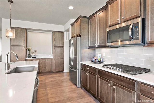 kitchen with stainless steel appliances, a sink, backsplash, light countertops, and light wood-type flooring