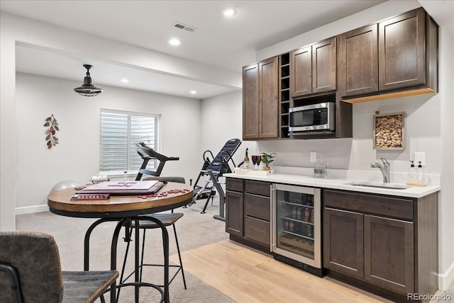 bar featuring beverage cooler, visible vents, stainless steel microwave, a sink, and wet bar