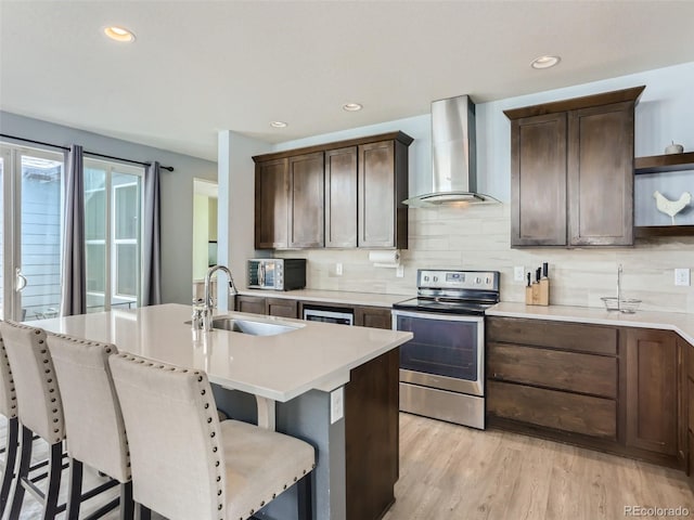 4628 Mt Shavano St, Brighton, CO 80601 - kitchen featuring stainless steel electric range oven, wall chimney range hood, open shelves, a center island with sink, and light countertops