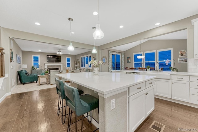 6470 Amur Ct, Castle Rock, CO 80108 - kitchen featuring wood finished floors, a kitchen island, white cabinets, light countertops, and lofted ceiling