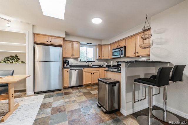 kitchen featuring kitchen peninsula, stainless steel appliances, light brown cabinets, a kitchen bar, and sink